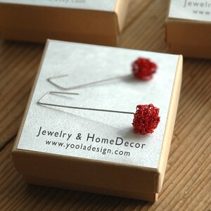 May include: A pair of red wire earrings in the shape of a flower bud. The earrings are displayed on a small brown box with the text "Jewelry & Home Decor www.yooladesign.com".