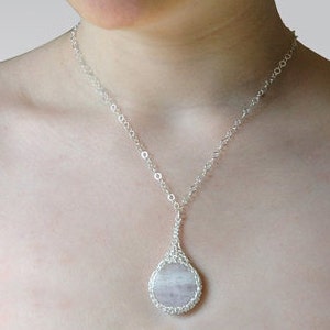 May include: A silver chain necklace with a teardrop-shaped pendant featuring a round, light pink and white gemstone.