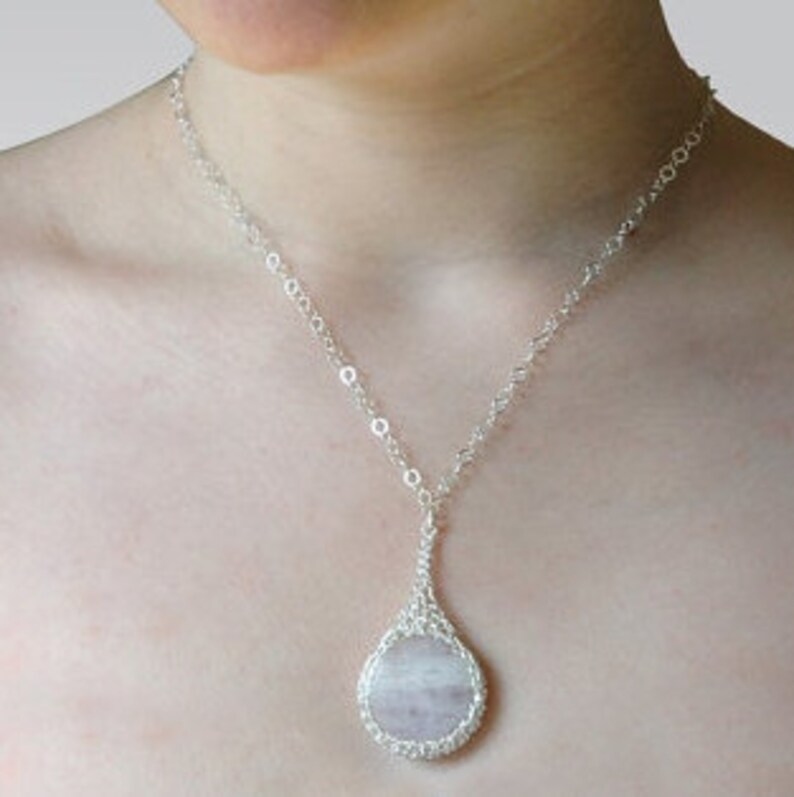 May include: A silver chain necklace with a teardrop-shaped pendant featuring a round, light pink and white gemstone.