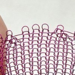 May include: A close-up of a pink metal chainmail mesh fabric. The fabric is woven in a tight, intricate pattern, creating a delicate and flexible material.