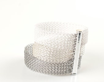 May include: A silver bracelet with a graduated ombre design, featuring a silver clasp. The bracelet is made of a delicate, woven mesh.