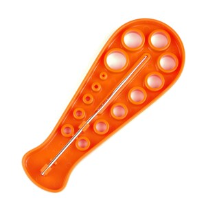 May include: Orange plastic crochet hook gauge with a metal needle. The gauge has 12 round holes of different sizes.