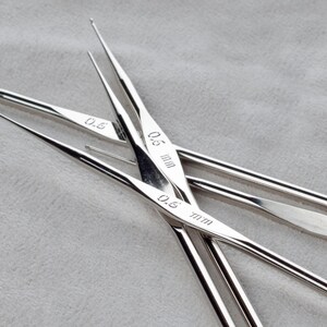 May include: A set of four silver knitting needles with the sizes 0.5 mm and 0.6 mm marked on them.