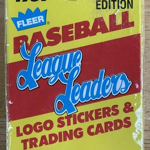 Puede incluir: Una caja amarilla y roja con una pegatina de logo de Fleer Baseball League Leaders de 1989 y tarjetas coleccionables. La caja dice "Edición limitada" y "6 pegatinas de logo y 44 tarjetas coleccionables".