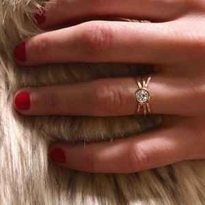 May include: A gold ring with a single, round, clear gemstone set in a bezel setting. The ring has a delicate, twisted band.