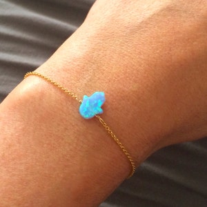 May include: A delicate gold chain bracelet with a light blue opal hamsa hand charm.