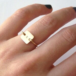 Può includere: Un anello d'oro con un'etichetta quadrata su cui è incisa la lettera "G".