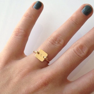 May include: A gold ring with a square-shaped tag that has the letter "C" engraved on it.