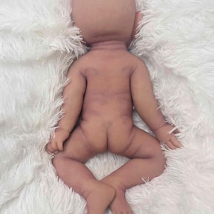 May include: A lifelike, anatomically correct baby doll with a bald head and realistic skin tones. The doll is lying on its back with its legs spread and arms slightly outstretched. The doll's skin has subtle shading and details.
