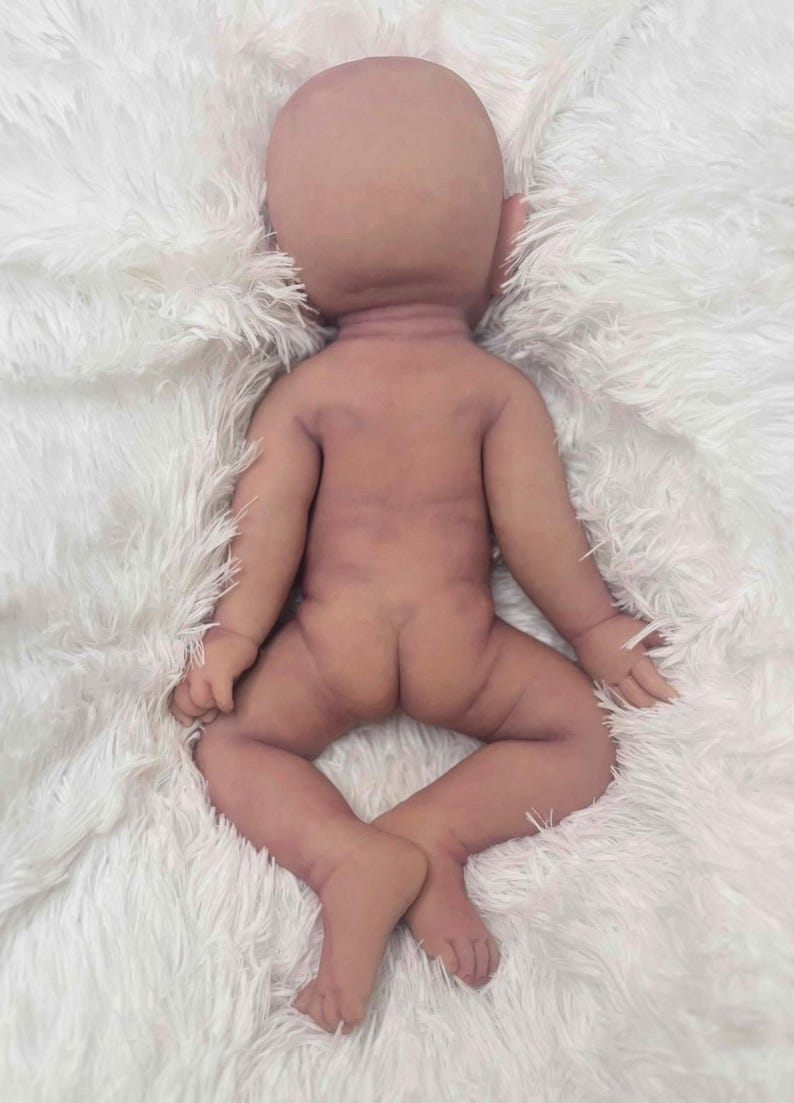 May include: A lifelike, anatomically correct baby doll with a bald head and realistic skin tones. The doll is lying on its back with its legs spread and arms slightly outstretched. The doll's skin has subtle shading and details.
