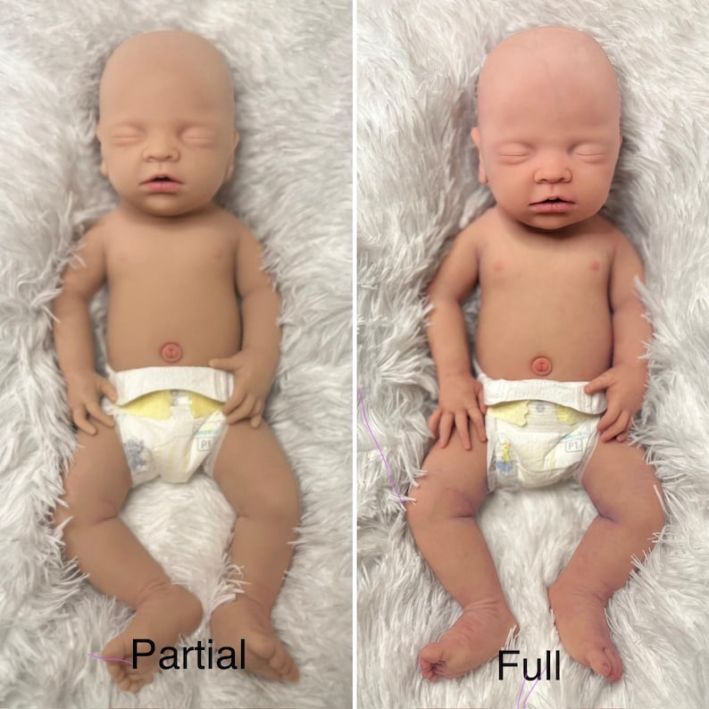 K&ouml;nnte beinhalten: Zwei realistische Babypuppen, eine mit der Aufschrift "Partial" und die andere mit "Full". Beide Puppen sind nackt, mit geschlossenen Augen und tragen Windeln. Die Puppen liegen auf einer wei&szlig;en, flauschigen Oberfl&auml;che. Die Puppen haben eine br&auml;unliche Hautfarbe.