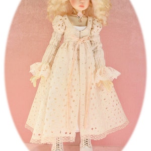 May include: A doll with blonde curly hair wearing a white dress with a pink ribbon and white shoes. The doll has pointed ears and is wearing a flower crown.