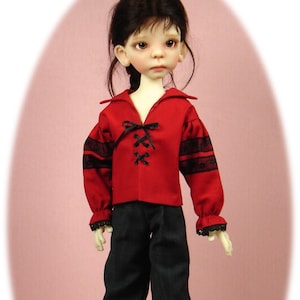May include: A doll wearing a red shirt with black lace trim and black pants. The doll has long brown hair and is wearing black boots.