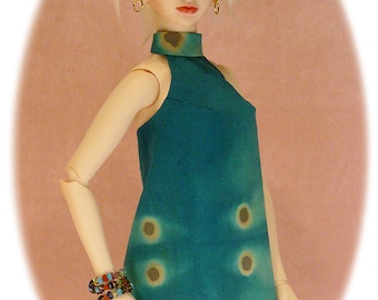 May include: A doll wearing a teal blue dress with brown accents. The dress has a high neckline and a sleeveless design. The doll has white hair and is wearing gold earrings.