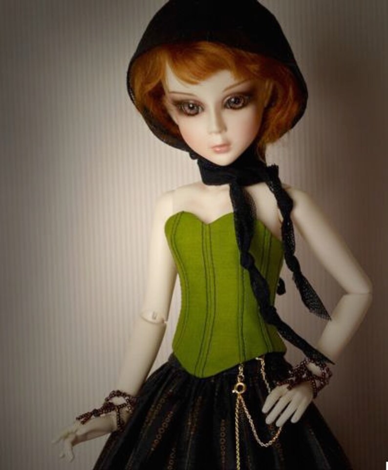 May include: A doll with red hair wearing a black hooded top, a green corset, and a black and gold skirt.