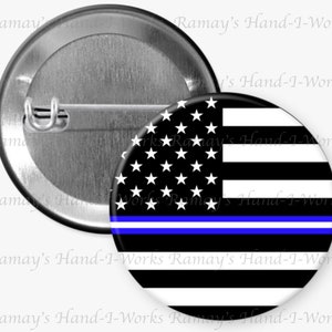 May include: A black and white American flag with a thin blue line across the middle. The flag is on a round button.