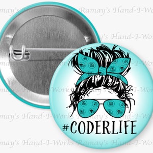 May include: A turquoise blue button with a black and white illustration of a woman with a messy bun wearing sunglasses. The woman's hair is tied with a turquoise blue bandana with a pattern of medical symbols. The text "#CODERLIFE" is printed in black below the illustration.