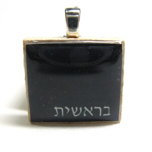May include: A black square pendant with a silver bail. The pendant has the Hebrew words "בר אשי" written in white on the front.