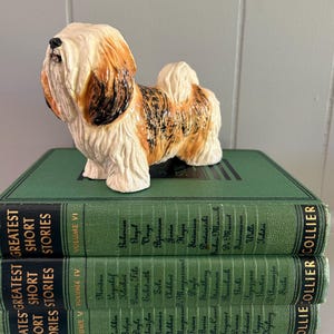 May include: A ceramic dog figurine with a white, brown, and black coat stands atop three green hardcover books. The books are titled "Greatest Short Stories" and are labeled with volume numbers.