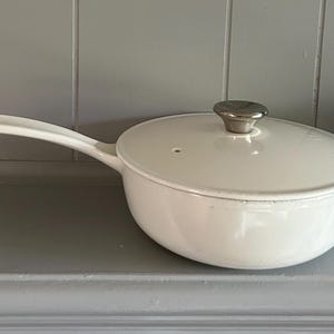 May include: White enameled cast iron saucepan with a lid and a silver knob. The saucepan has a long handle.