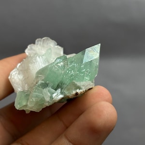 May include: A raw mineral specimen featuring a cluster of translucent, pale green crystalline points attached to a base of opaque, white, textured mineral formations. The structure displays sharp, angular facets and a natural, unpolished appearance.