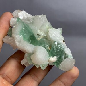 May include: A mineral specimen featuring a cluster of translucent, pale green crystals interspersed with opaque, white, fibrous crystal formations. The structure is irregular and jagged, showcasing a contrast between the smooth green surfaces and the textured white mineral deposits throughout the piece.