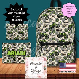 Puede incluir: Una mochila y dos estuches a juego con un patrón de motos de cross verdes, banderas a cuadros, rayos y el texto BRAAAP. Un estuche muestra el nombre ARIANI en verde. El texto incluye Backpack with matching zipper pouches, Customize it with your name or initials, Pancake & Moose y MADE IN USA.