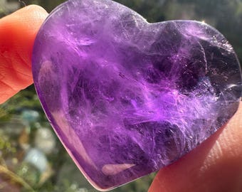 May include: A heart-shaped amethyst crystal with a deep purple hue and intricate patterns. The crystal is polished and smooth, with a translucent appearance.