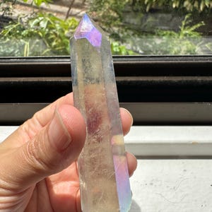 Op de afbeelding: Een heldere kwartskristalpunt met iriserende regenboogkleuren. De kristal is ongeveer 12,5 cm lang en heeft een puntige punt.
