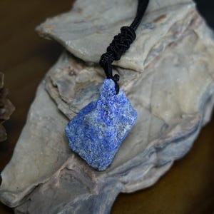 May include: A dark blue lapis lazuli stone pendant on a black cord. The stone is rough and has a natural, irregular shape.