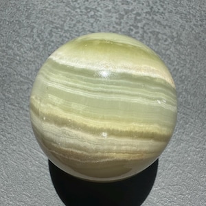 May include: A green and white striped sphere made of polished stone. The sphere has a smooth, glossy finish.