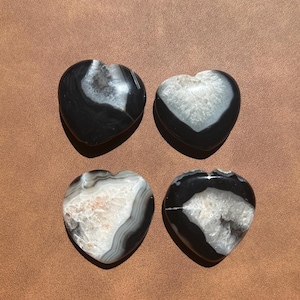 May include: Four black and white agate heart-shaped stones. The stones have a natural, polished finish and are arranged in a grid pattern.
