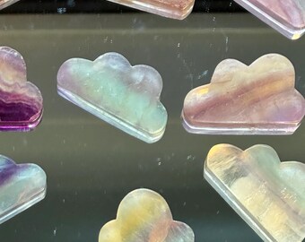 May include: A collection of nine iridescent rainbow fluorite cloud shaped crystal carvings. The crystals are translucent and have a variety of colors, including purple, pink, green, and yellow.
