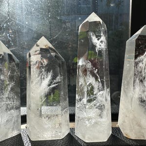 Könnte beinhalten: Vier klare Quarz-Kristallspitzen mit unterschiedlichen Höhen und Formen. Die Kristalle sind transparent mit inneren Adern und Facetten, die das Licht reflektieren. Sie sind in einer Reihe angeordnet und zeigen ihre natürliche Schönheit.