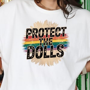 Könnte beinhalten: Weißes T-Shirt mit einer Regenbogengrafik und dem Text "Protect the Dolls" in schwarzen Buchstaben.