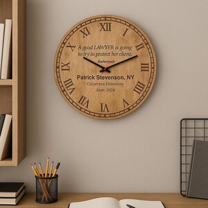 Puede incluir: Un reloj de madera redondo con números romanos y manecillas negras. El reloj presenta texto grabado: "A good LAWYER is going to try to protect her client." El texto adicional incluye un nombre, una ubicación y una fecha.