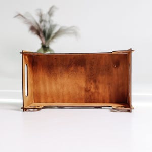 May include: A wooden box with a light brown stain. The box is empty and has a rectangular shape. The box has a small handle on the side.