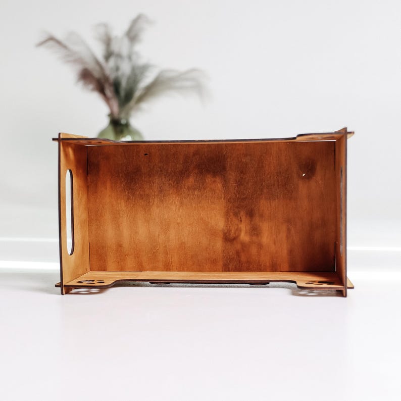 May include: A wooden box with a light brown stain. The box is empty and has a rectangular shape. The box has a small handle on the side.