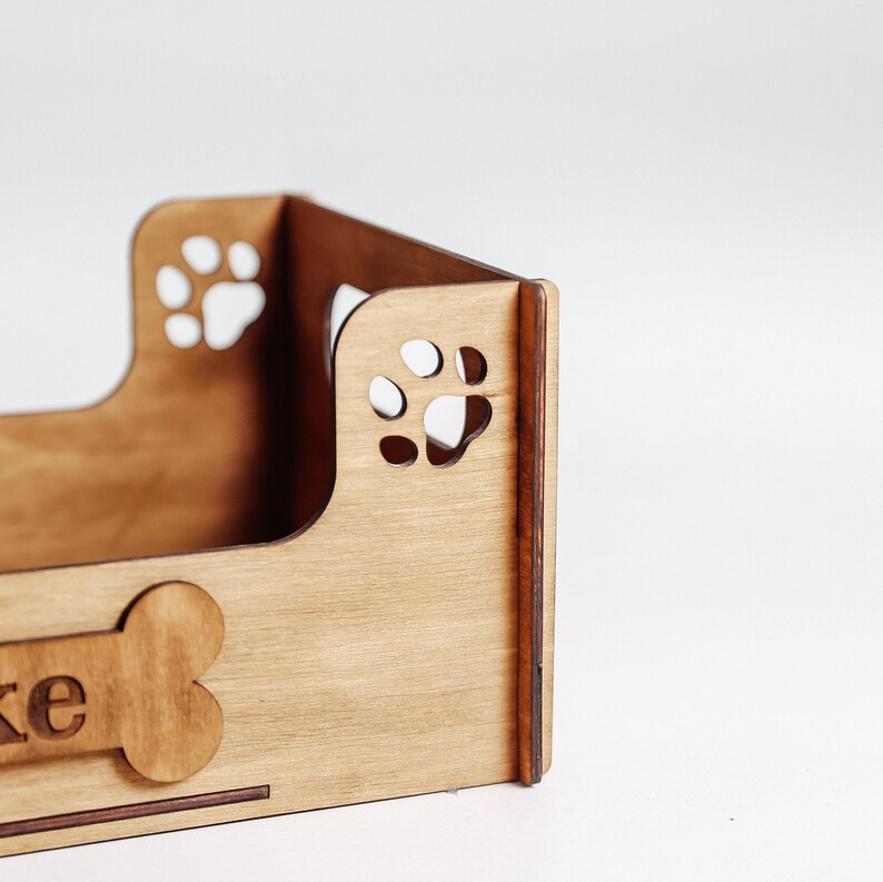 May include: A light brown wooden dog bed with a paw print design and the name "Ike" engraved on the front.