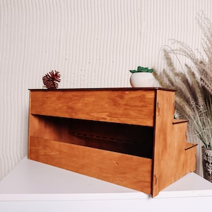 Pode incluir: Um expositor de madeira de tr&ecirc;s n&iacute;veis. O expositor &eacute; feito de madeira natural e tem um acabamento marrom claro. O expositor &eacute; perfeito para exibir itens pequenos, como joias, velas ou plantas.