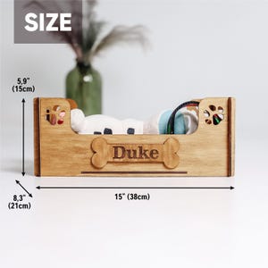 May include: Wooden dog bed with a bone-shaped nameplate that says "Duke". The bed is 15 inches long and 8.3 inches wide.