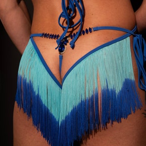 Puede incluir: Un bikini de abajo con flecos azul y turquesa con un adorno de joyas.