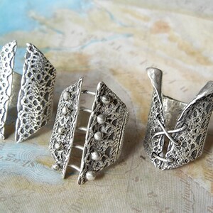May include: Three silver rings with intricate designs. The rings are made of textured metal and have different shapes and patterns.