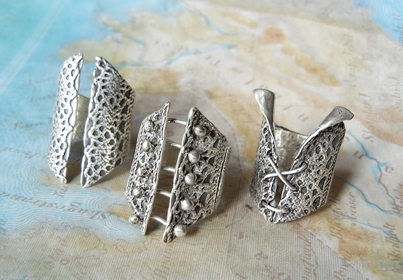 May include: Three silver rings with intricate designs. The rings are made of textured metal and have different shapes and patterns.