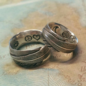 May include: Two silver rings with a feather design. The rings have peace signs and hearts engraved on them.
