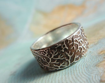 Puede incluir: Un anillo de plata con un diseño texturizado de ramas. El anillo es ancho y tiene un interior de plata pulida.