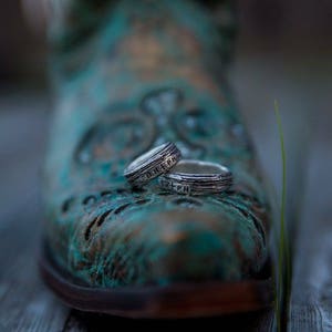 May include: Two silver rings with engraved details are resting on a blue and green patterned boot. The rings are stacked on top of each other.