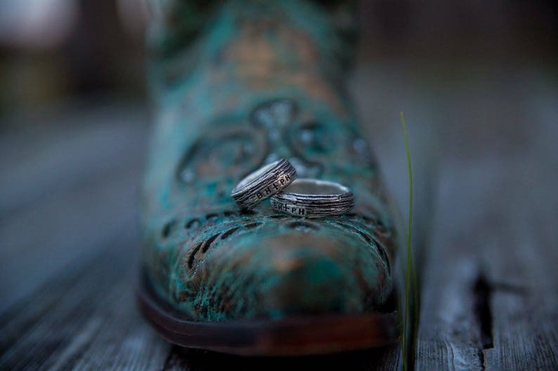 May include: Two silver rings with engraved details are resting on a blue and green patterned boot. The rings are stacked on top of each other.