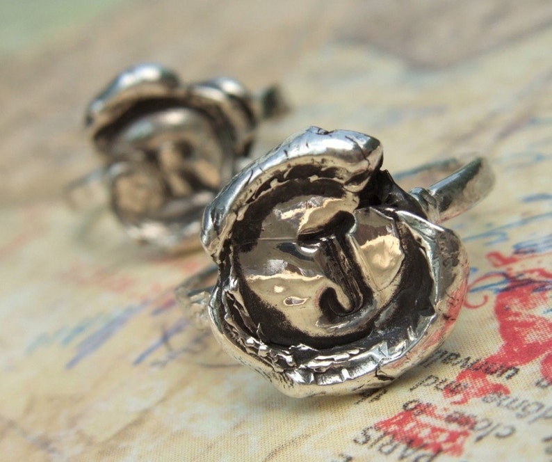 May include: Two silver rings with a wax seal design. The rings feature the letters "R" and "J" embossed in the center of the wax seal.