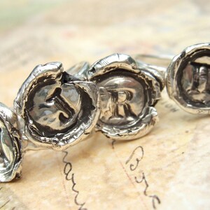 May include: Three silver rings with raised letters, J, R, and H, set in a wax seal design.